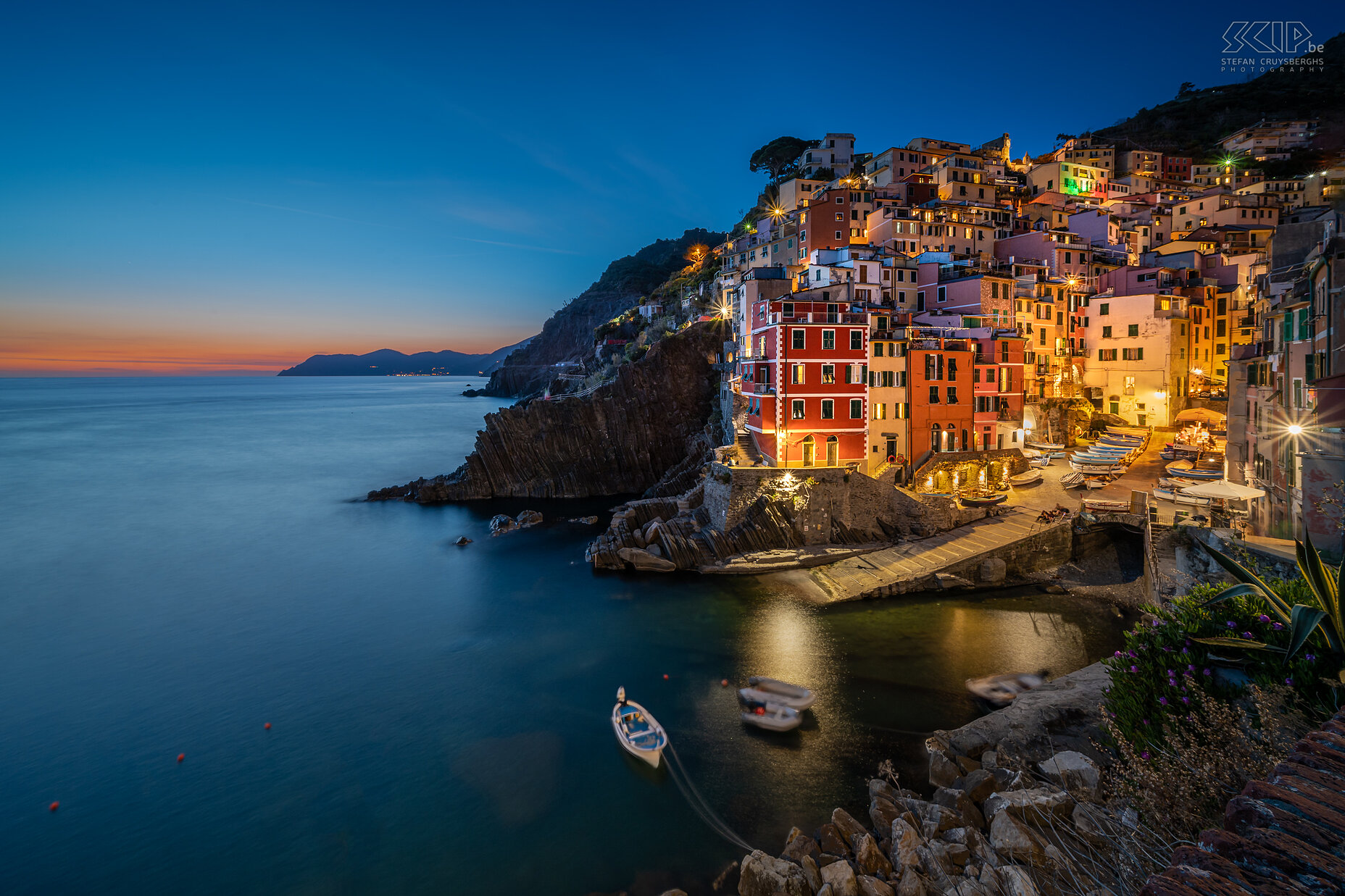 Riomaggiore - By night Riomaggiore is het meest zuidelijke dorp. Het ligt diep ingesneden tussen de heuvels, waarop terrassen zijn aangelegd voor de landbouw. De huizen hebben de typisch Ligurische kleuren (rood, roze, oker) en leunen tegen de helling aan. Riomaggiore telt zo'n 2.000 inwoners en is daarmee met Monterosso het grootste dorp. Het dorp ontstond al in de twaalfde eeuw. Stefan Cruysberghs